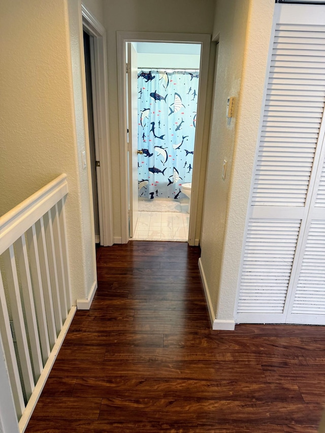 corridor featuring baseboards, a textured wall, and wood finished floors