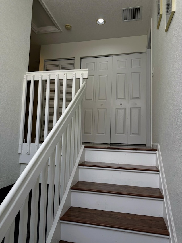 stairway with recessed lighting, a textured wall, and visible vents