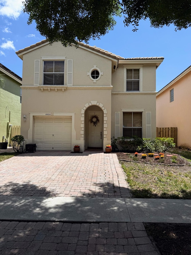 mediterranean / spanish house with fence, decorative driveway, stucco siding, an attached garage, and a tile roof