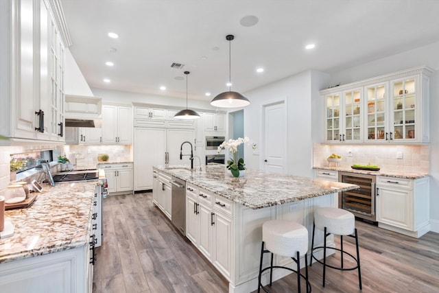 10343 S Barnsley Dr, Parkland, FL 33076 - kitchen with wine cooler, stainless steel appliances, backsplash, white cabinets, and light wood-type flooring