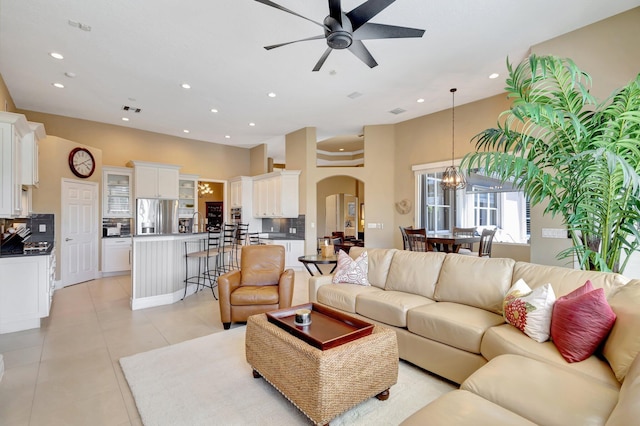 living area with arched walkways, recessed lighting, light tile patterned flooring, and ceiling fan with notable chandelier