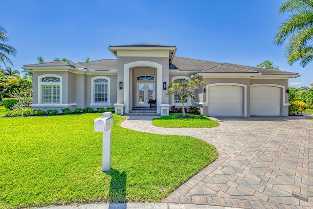 mediterranean / spanish-style house with french doors, a front yard, decorative driveway, an attached garage, and stucco siding
