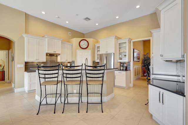 kitchen featuring a breakfast bar area, visible vents, dark countertops, white cabinets, and freestanding refrigerator