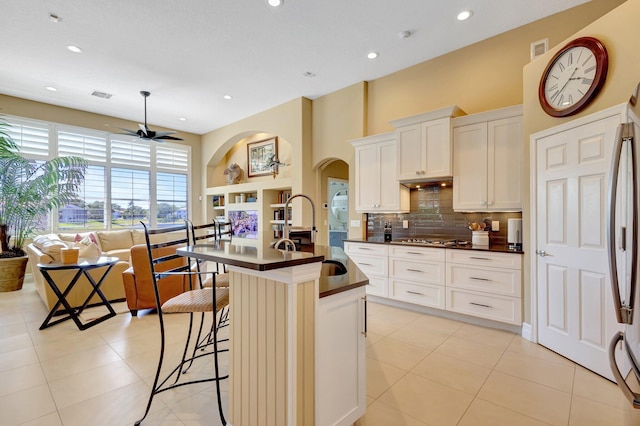 kitchen with ceiling fan, backsplash, dark countertops, arched walkways, and a sink