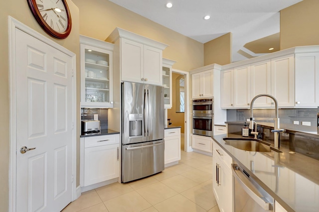 kitchen with light tile patterned flooring, glass insert cabinets, tasteful backsplash, a sink, and stainless steel appliances