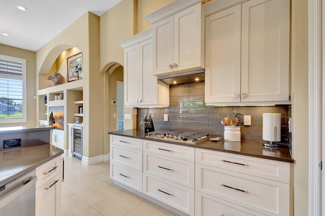kitchen featuring dark countertops, appliances with stainless steel finishes, arched walkways, light tile patterned floors, and backsplash