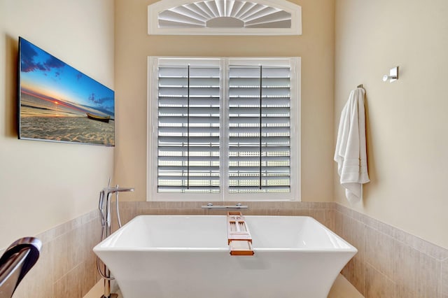 bathroom with tile walls, wainscoting, and a soaking tub