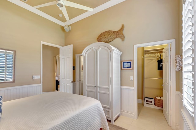bedroom with light tile patterned floors, a wainscoted wall, a closet, a spacious closet, and a high ceiling