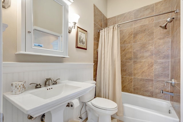 bathroom with toilet, wainscoting, and shower / bath combo with shower curtain