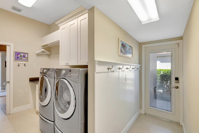 clothes washing area featuring independent washer and dryer, light tile patterned flooring, visible vents, and cabinet space