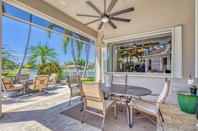 view of patio with a ceiling fan, fence, a water view, and outdoor dining space