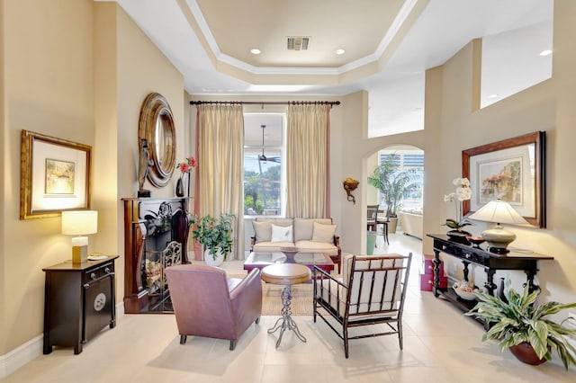 living area featuring visible vents, a high ceiling, a tray ceiling, arched walkways, and light tile patterned floors