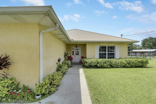 doorway to property with stucco siding, metal roof, and a lawn