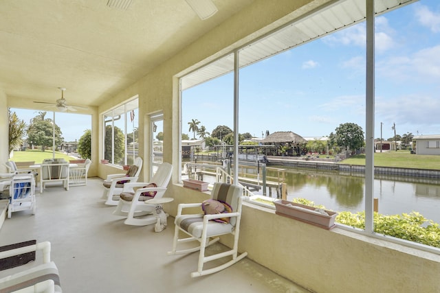 sunroom with concrete floors, a ceiling fan, and a water view