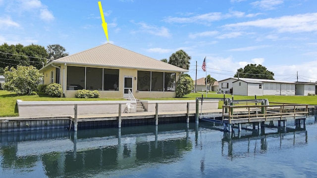 back of property with a water view, metal roof, boat lift, a lawn, and a sunroom