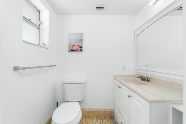 half bathroom with tile patterned flooring, vanity, toilet, baseboards, and visible vents