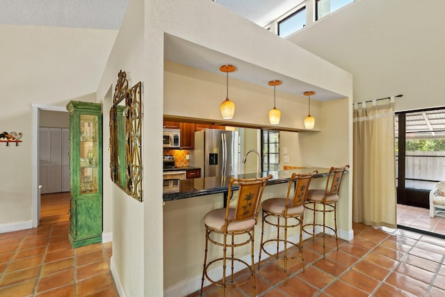 kitchen featuring stainless steel appliances, baseboards, a kitchen breakfast bar, and a towering ceiling