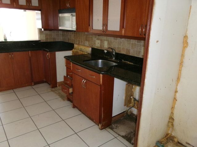 kitchen with a sink, dark countertops, white microwave, decorative backsplash, and brown cabinets