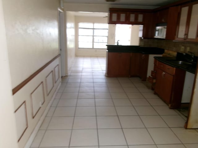 kitchen with dark countertops, glass insert cabinets, light tile patterned floors, and a sink