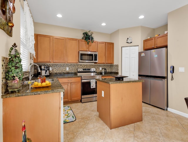 kitchen featuring appliances with stainless steel finishes, tasteful backsplash, a center island, a sink, and dark stone countertops