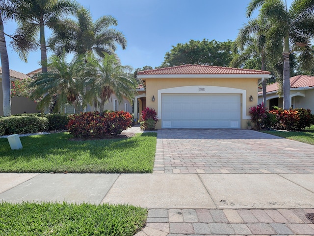 mediterranean / spanish home featuring a front lawn, decorative driveway, stucco siding, a tiled roof, and an attached garage