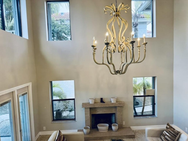 living room featuring a chandelier, a towering ceiling, a fireplace with raised hearth, and baseboards