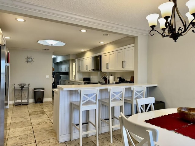 kitchen with crown molding, wall chimney exhaust hood, a peninsula, white cabinets, and a chandelier