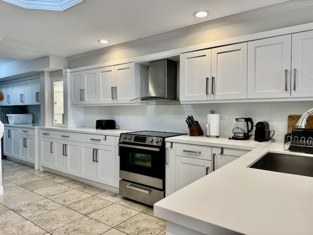 kitchen featuring wall chimney exhaust hood, stainless steel range with electric cooktop, backsplash, crown molding, and recessed lighting