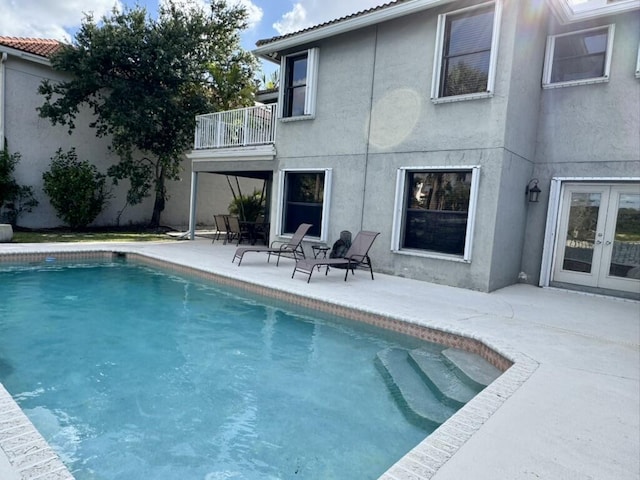 back of house with a balcony, french doors, a patio area, stucco siding, and an outdoor pool
