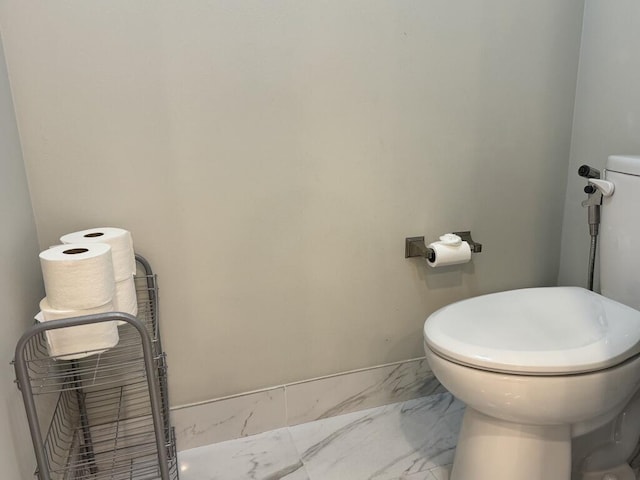 bathroom with toilet, marble finish floors, and baseboards