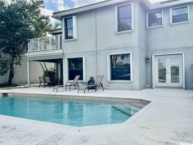 rear view of property featuring a balcony, a patio area, an outdoor pool, and stucco siding