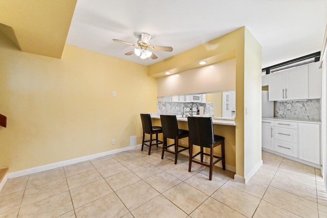 kitchen with backsplash, light tile patterned flooring, a kitchen bar, and ceiling fan