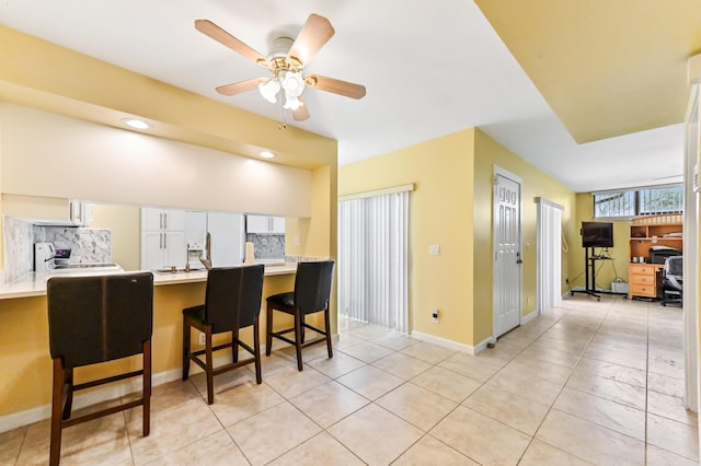 kitchen featuring stove, a kitchen breakfast bar, backsplash, a ceiling fan, and light tile patterned floors