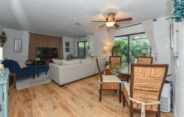 living room featuring a ceiling fan, a textured ceiling, visible vents, and light wood-type flooring