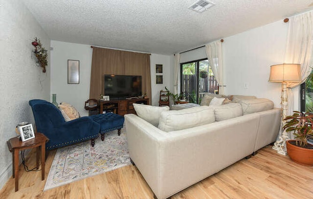 living room with light wood-style flooring, visible vents, and a textured ceiling