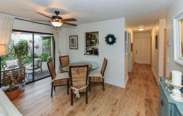 dining space featuring light wood-type flooring, baseboards, a textured ceiling, and ceiling fan