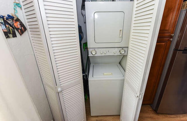 laundry room featuring stacked washer and clothes dryer, wood finished floors, and laundry area