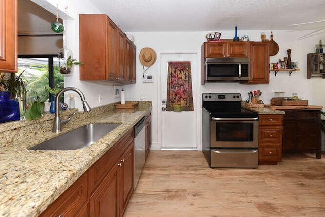 kitchen featuring a textured ceiling, a sink, stainless steel appliances, light wood finished floors, and light stone countertops