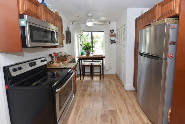 kitchen with light wood-type flooring, ceiling fan, brown cabinets, and appliances with stainless steel finishes
