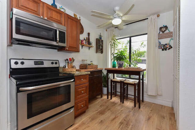 kitchen featuring light wood-type flooring, a ceiling fan, brown cabinets, and appliances with stainless steel finishes