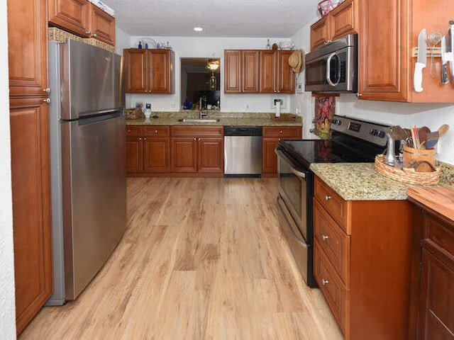 kitchen featuring brown cabinetry, appliances with stainless steel finishes, a sink, and light wood-style floors