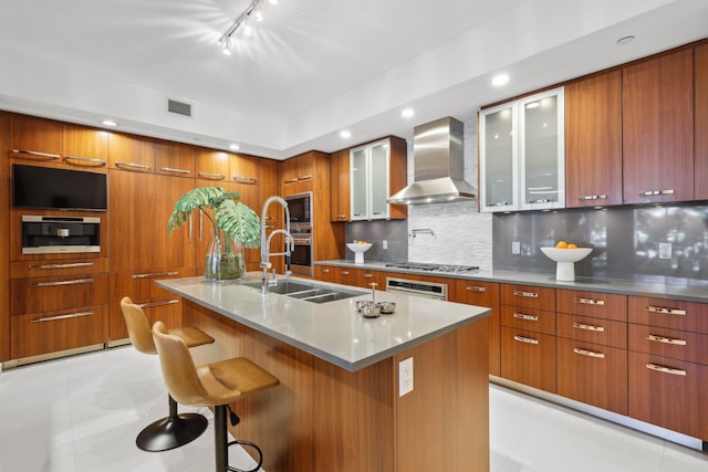 kitchen featuring visible vents, modern cabinets, wall chimney range hood, brown cabinetry, and appliances with stainless steel finishes