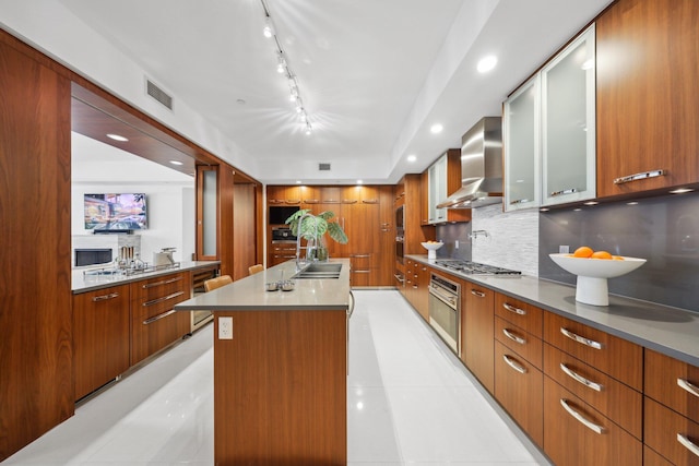 kitchen featuring brown cabinets, glass insert cabinets, modern cabinets, wall chimney exhaust hood, and visible vents