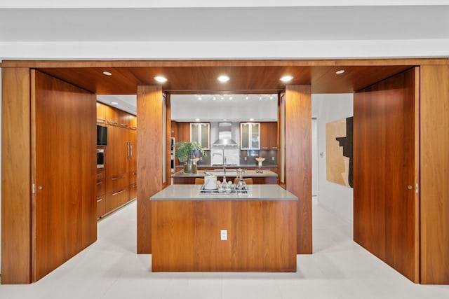 kitchen featuring tasteful backsplash, modern cabinets, brown cabinets, wall chimney range hood, and light countertops