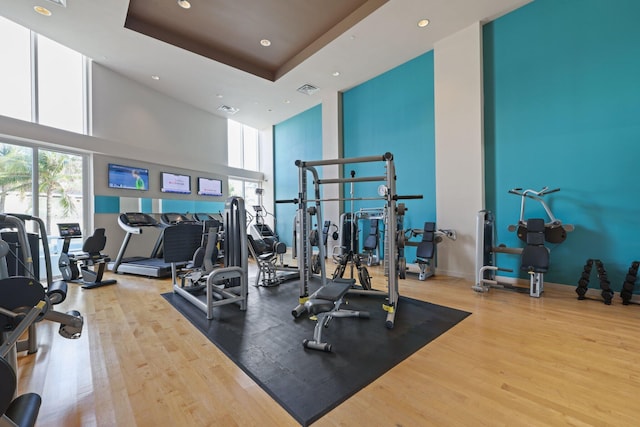 exercise room with a high ceiling, wood finished floors, visible vents, and recessed lighting
