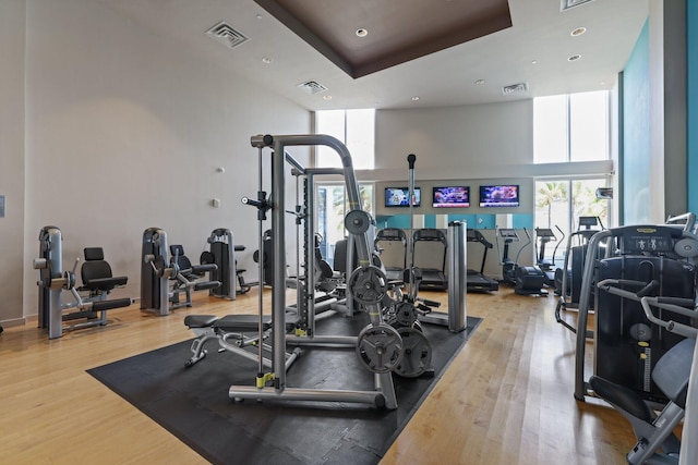 exercise room featuring wood finished floors, visible vents, and a towering ceiling