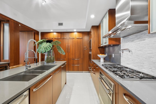 kitchen with a sink, visible vents, brown cabinets, wall chimney range hood, and appliances with stainless steel finishes