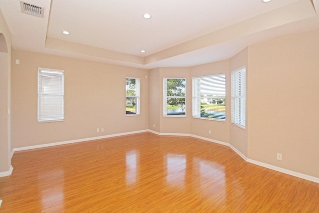 unfurnished room featuring light wood-style flooring, visible vents, recessed lighting, and a tray ceiling