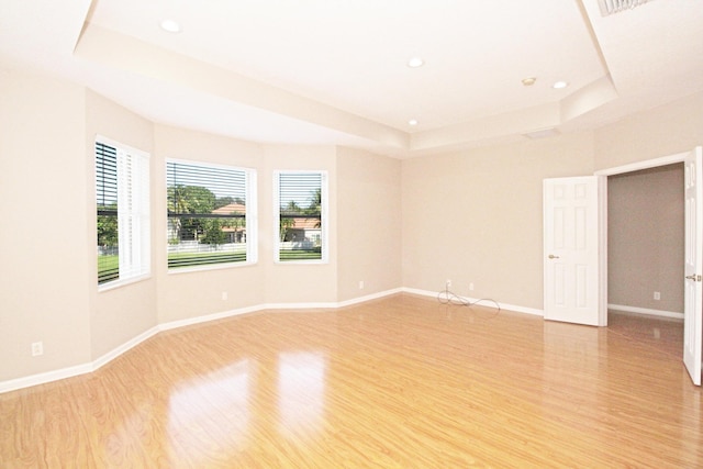 empty room featuring a tray ceiling, recessed lighting, and light wood-style floors
