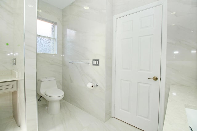 bathroom with marble finish floor, toilet, vanity, and tile walls